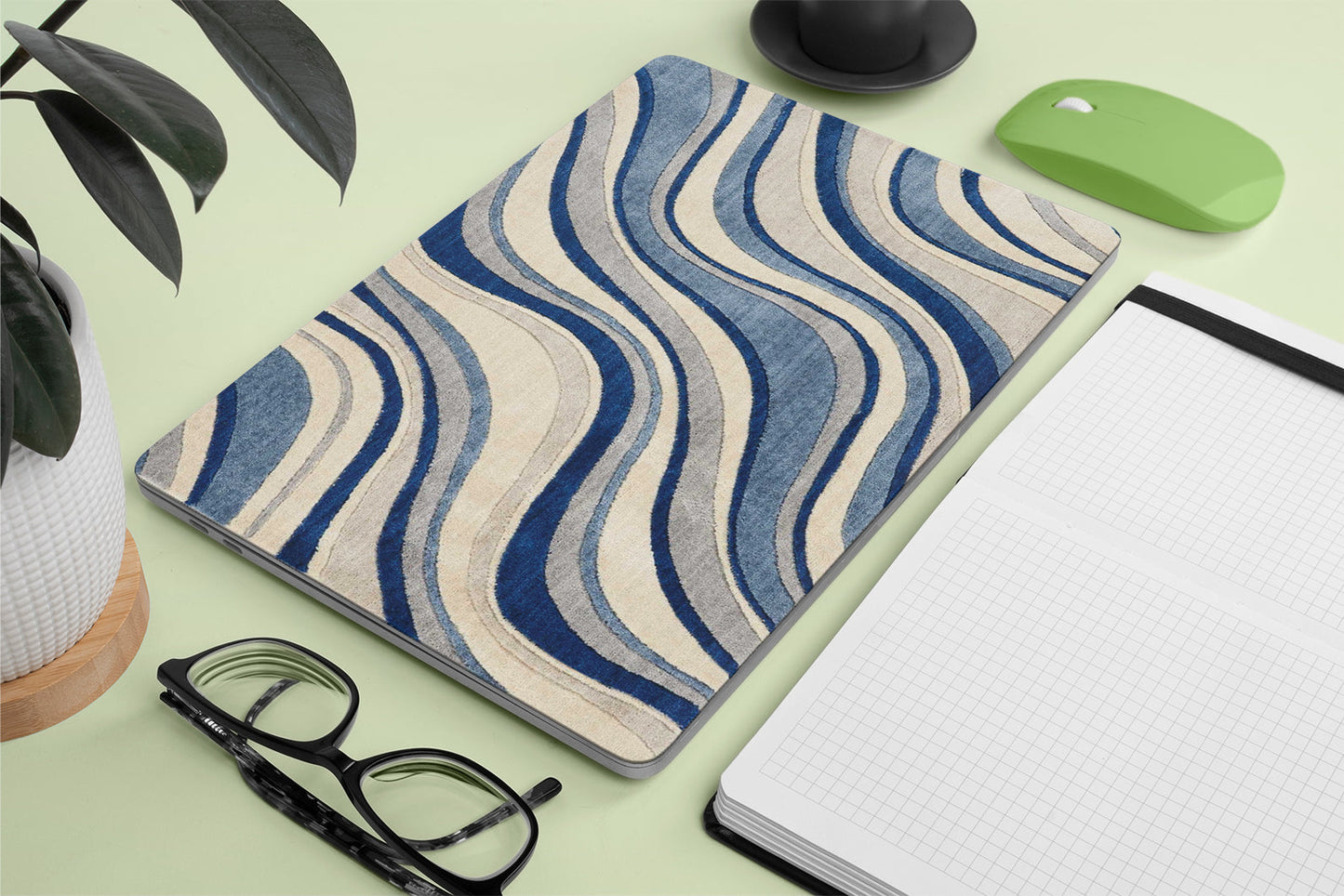Wavy patterned macbook skin on a desk with glasses, notebook, and plant