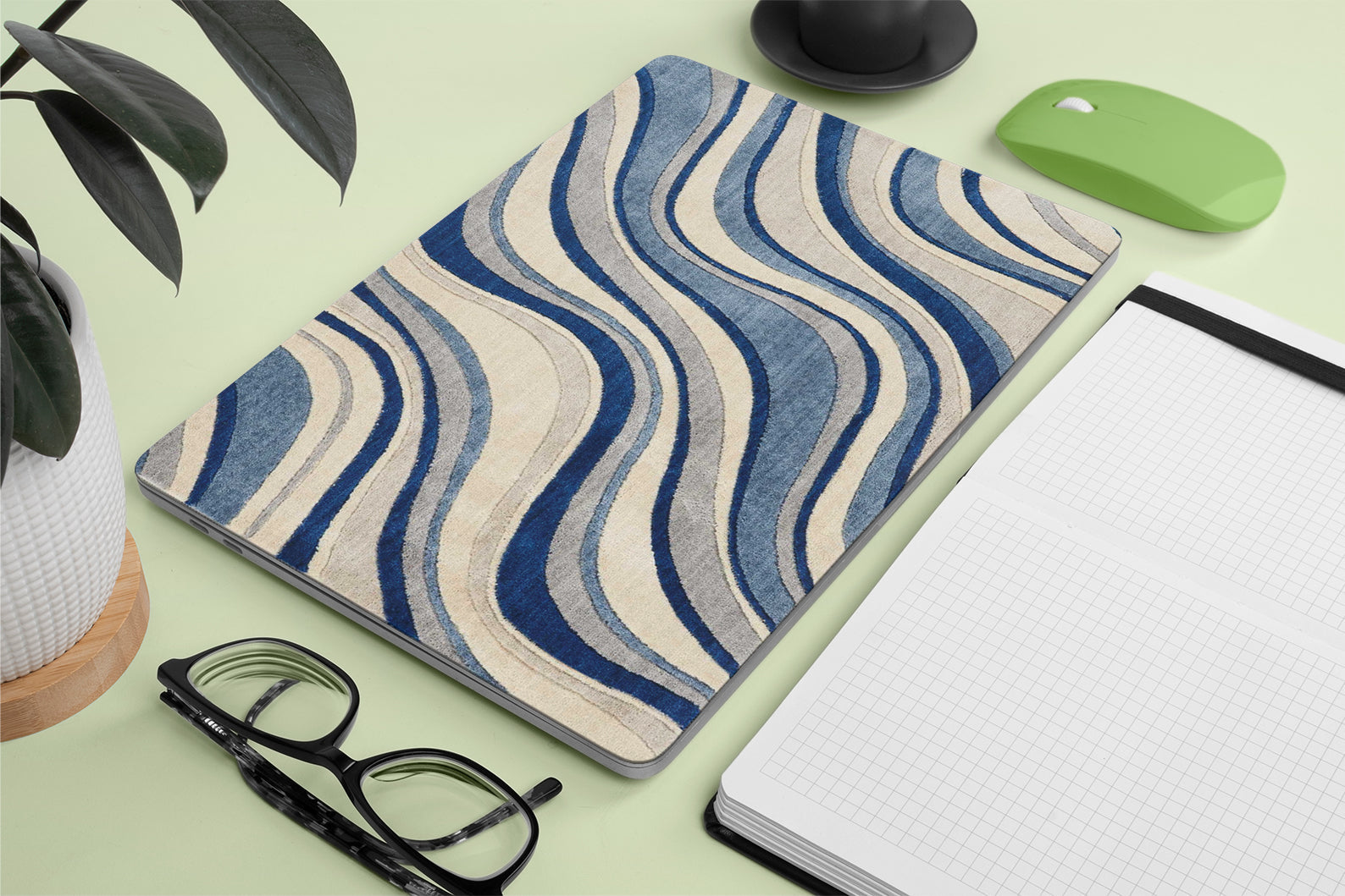 Wavy patterned macbook skin on a desk with glasses, notebook, and plant