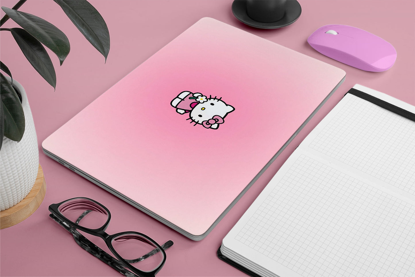 Pink laptop skin with Hello Kitty sticker on a pink surface with a plant, glasses, and mouse.