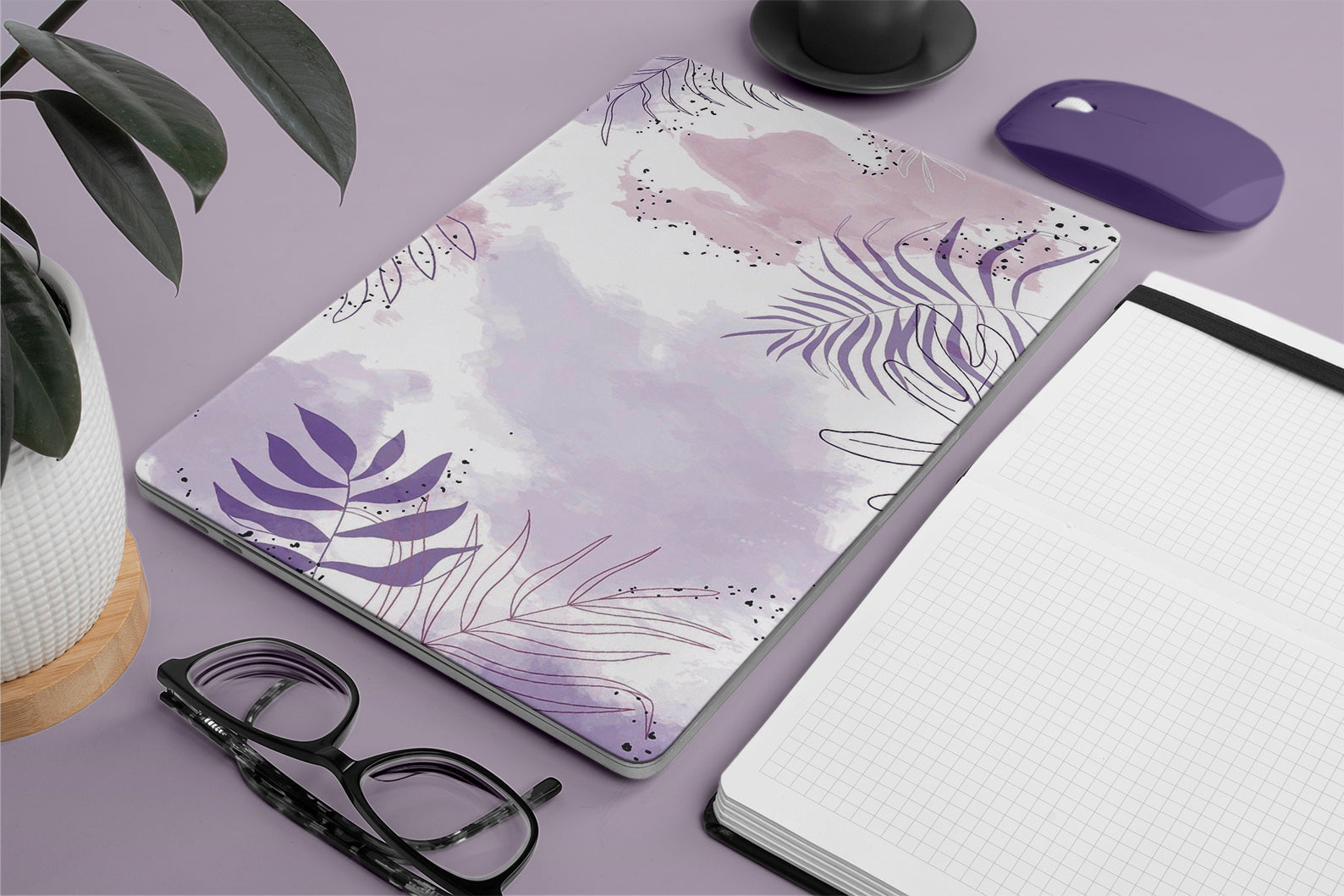 Floral design macbook on a desk with glasses, notebook, and mouse.